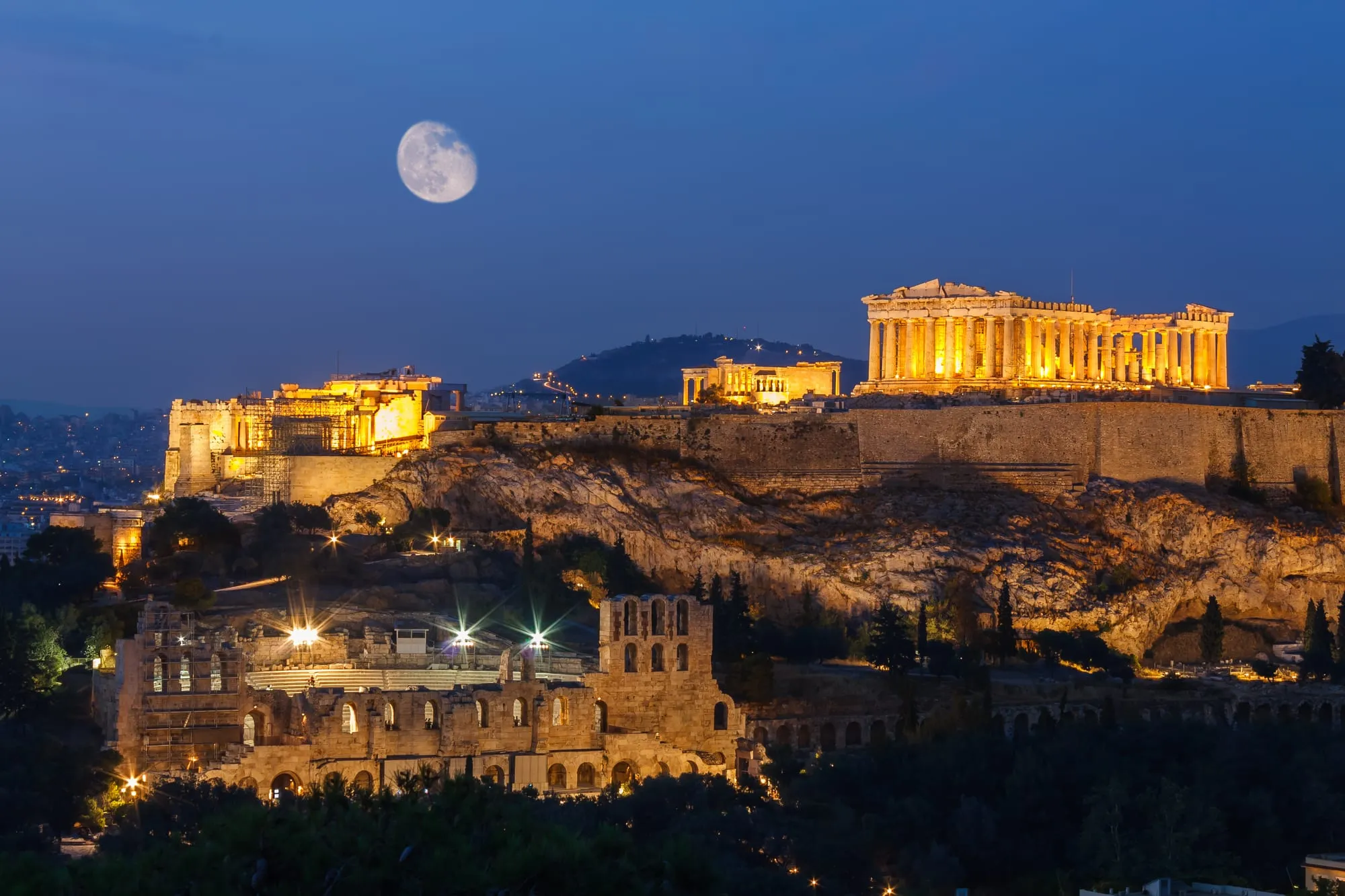 The Acropolis of Athens lit up at night under a full moon